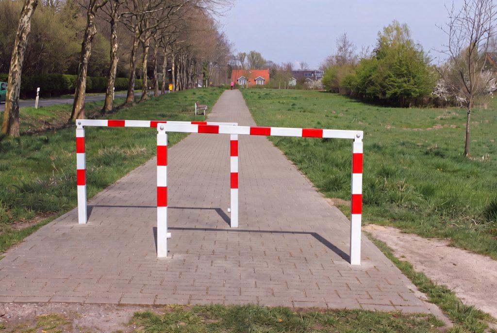 Herausnehmbare Wegesperre mit weißer Beschichtung und roter Reflexfolie auf einem gepflastertem Fußweg